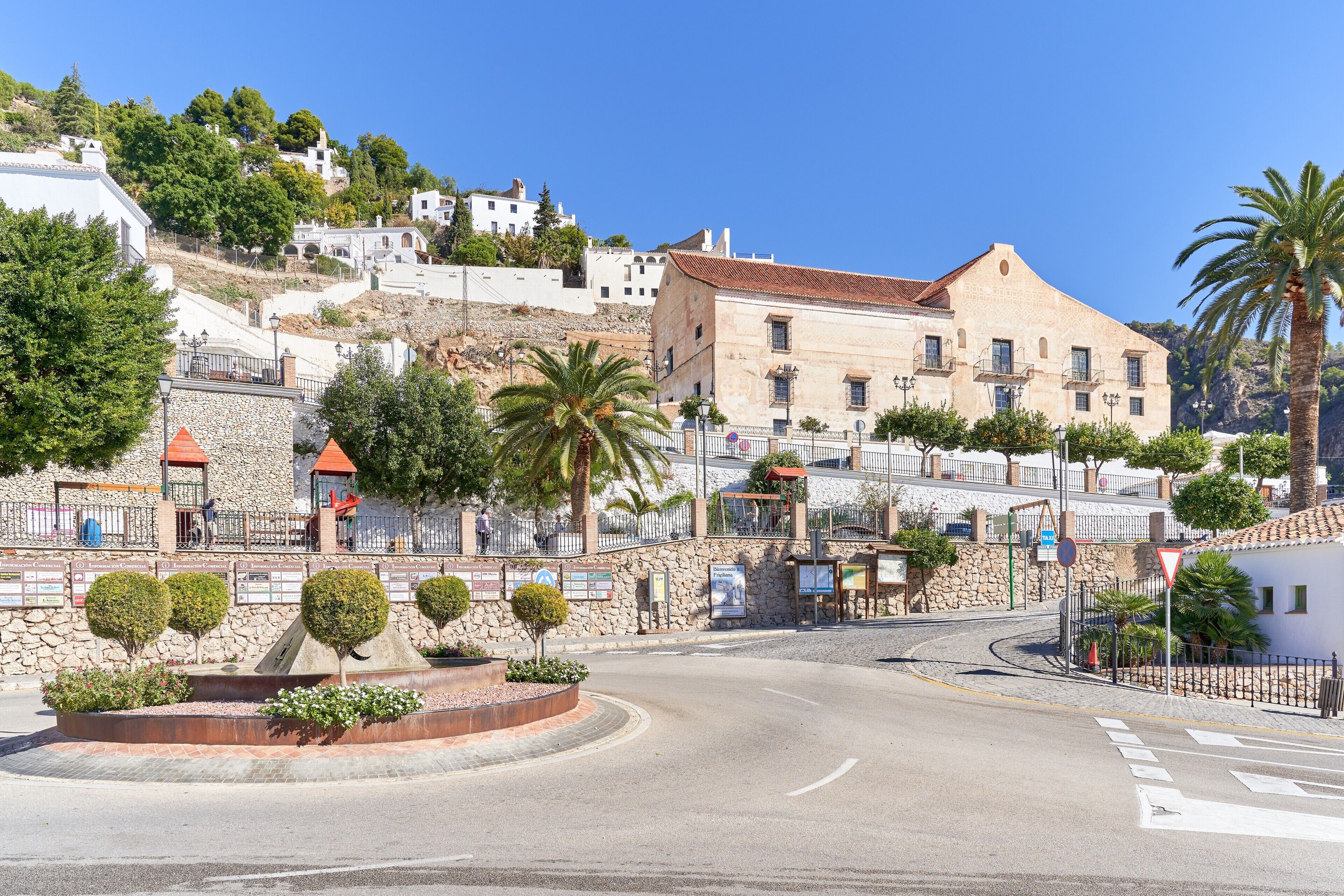 Una calle con una glorieta, edificios de piedra y una colina con casas blancas.