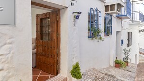 A white building with a wooden door, potted plants, and a tiled courtyard.