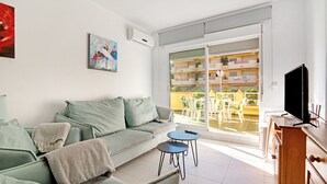 Ein Wohnzimmer mit einer Couch, einem kleinen Tisch, einem Fernseher und einem Balkon mit Gartenmöbeln.