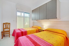 A bedroom with two beds, a wooden chair, a nightstand, and a sliding door.