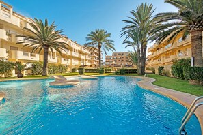A swimming pool surrounded by palm trees and multi-story buildings.