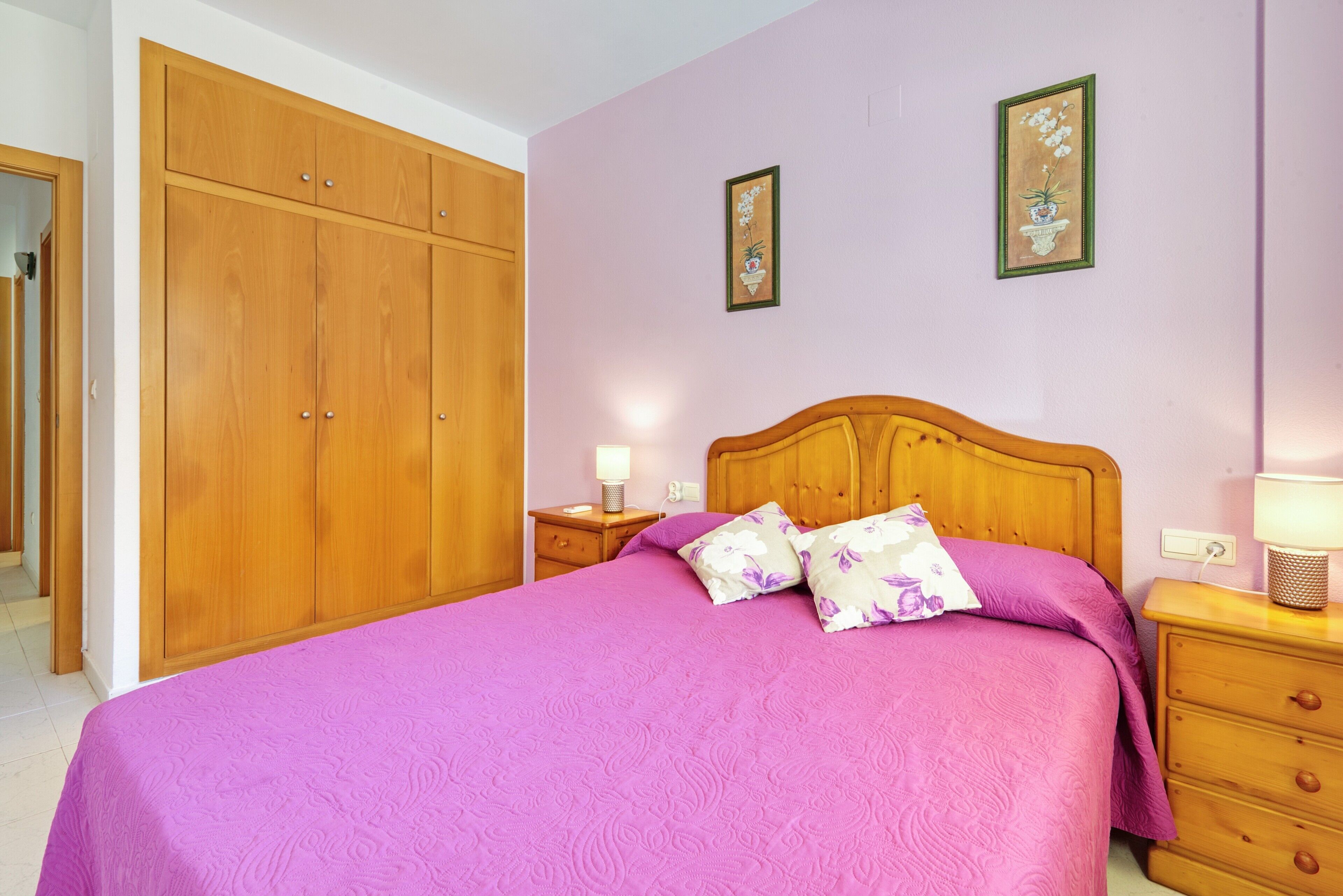 Un dormitorio con cama, armario de madera, mesitas de noche y un cuadro colgado en la pared.