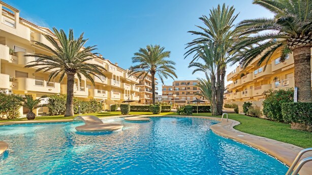 A swimming pool surrounded by palm trees and multi-story buildings. - Apartment "Brisas C2" with Shared Pool & Wi-Fi (Denia)