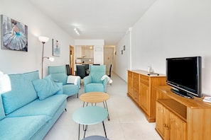 Een woonkamer met een bank, twee fauteuils, een salontafel, een televisie en een houten kast.
