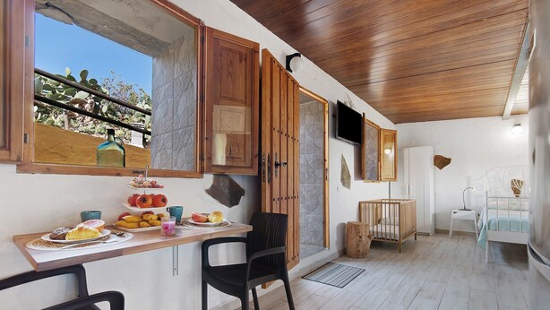 A kitchen with wooden cabinets, a dining table with chairs, a crib, and a television mounted on the wall. - Holiday Studio 'Maya' with Sea View, Private Terrace and Wi-Fi (Guia)