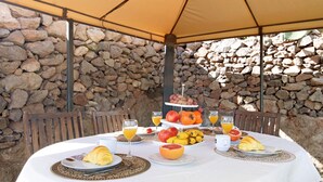 An outdoor dining area with a stone wall backdrop, a table set with breakfast items, and a three-tiered fruit display. - Holiday Studio 'Maya' with Sea View, Private Terrace and Wi-Fi (Guia)