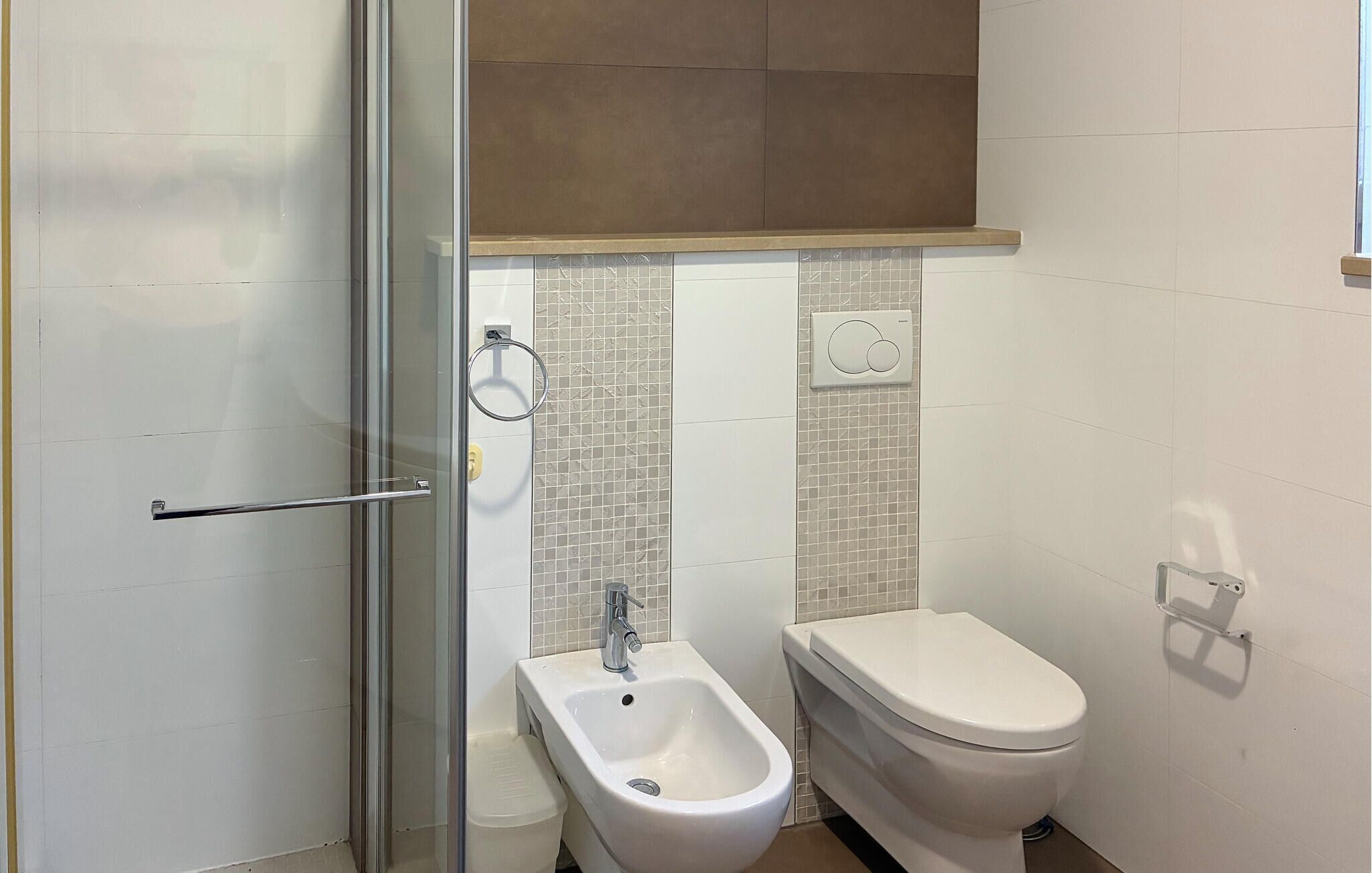 A bathroom with a glass shower enclosure, a bidet, a toilet, and a towel rack.