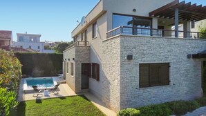 A modern two-story house with a stone facade, a swimming pool, and a covered patio area.
