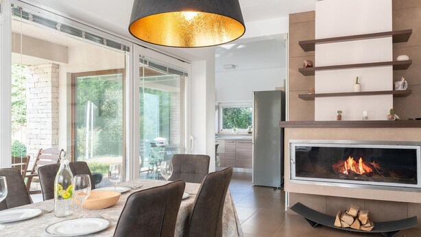 A modern dining area with a fireplace, a glass door leading to a patio, and a kitchen in the background.