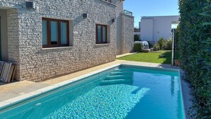 A swimming pool adjacent to a stone building with two windows, a clear blue pool, and a well-maintained lawn.