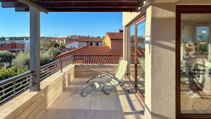 A balcony with a wooden floor, metal railing, and two lounge chairs.