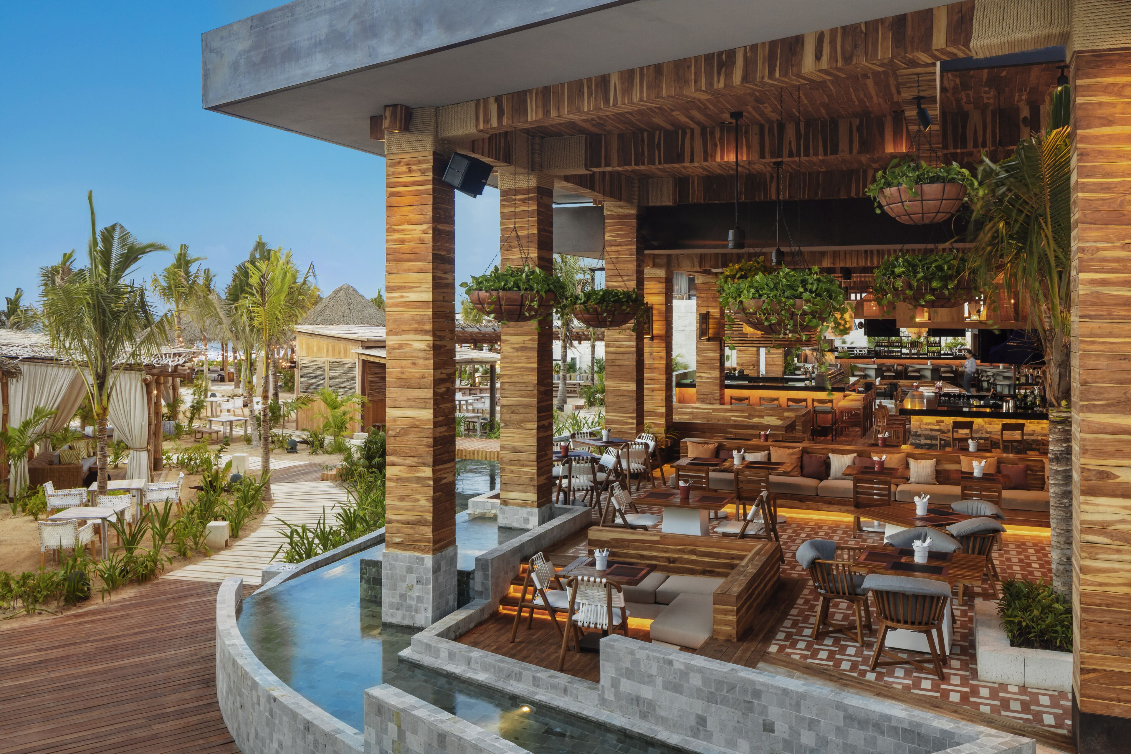 A modern outdoor lounge area with a pool, wooden pillars, and hanging planters.