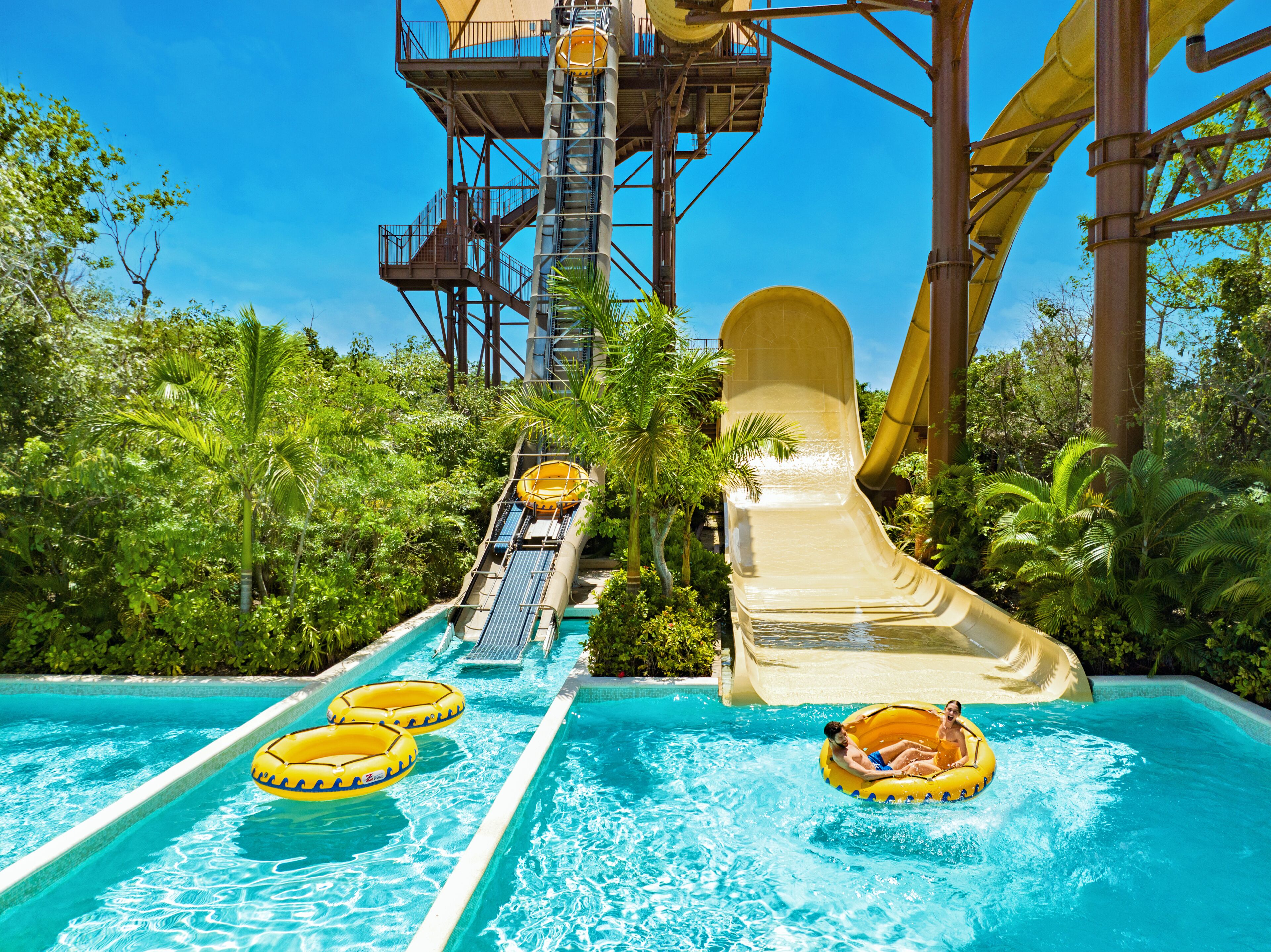 Ein Wasserpark mit einer großen Rutsche, mehreren Wasserrutschen und aufblasbaren Flößen in einem Pool.