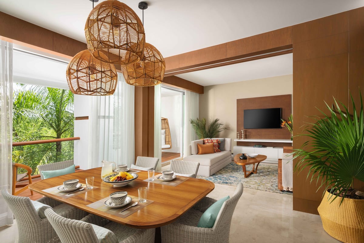 Un comedor moderno con una mesa de madera, sillas de mimbre y un ventanal con vistas a la vegetación.