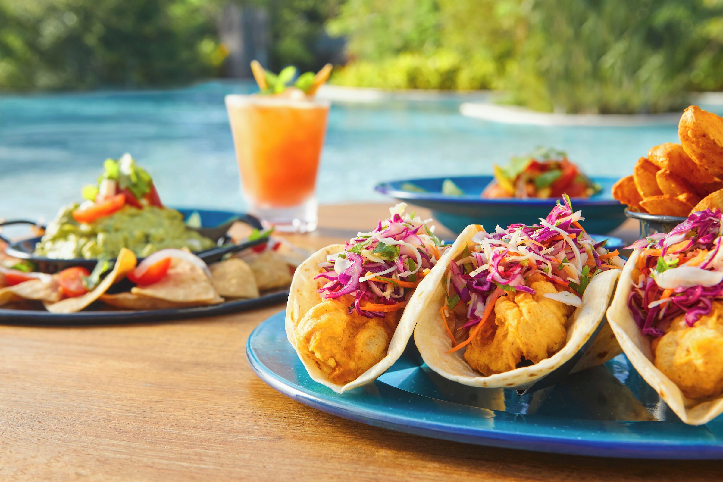 Una mesa con tres tacos, una bebida y un plato de papas fritas.