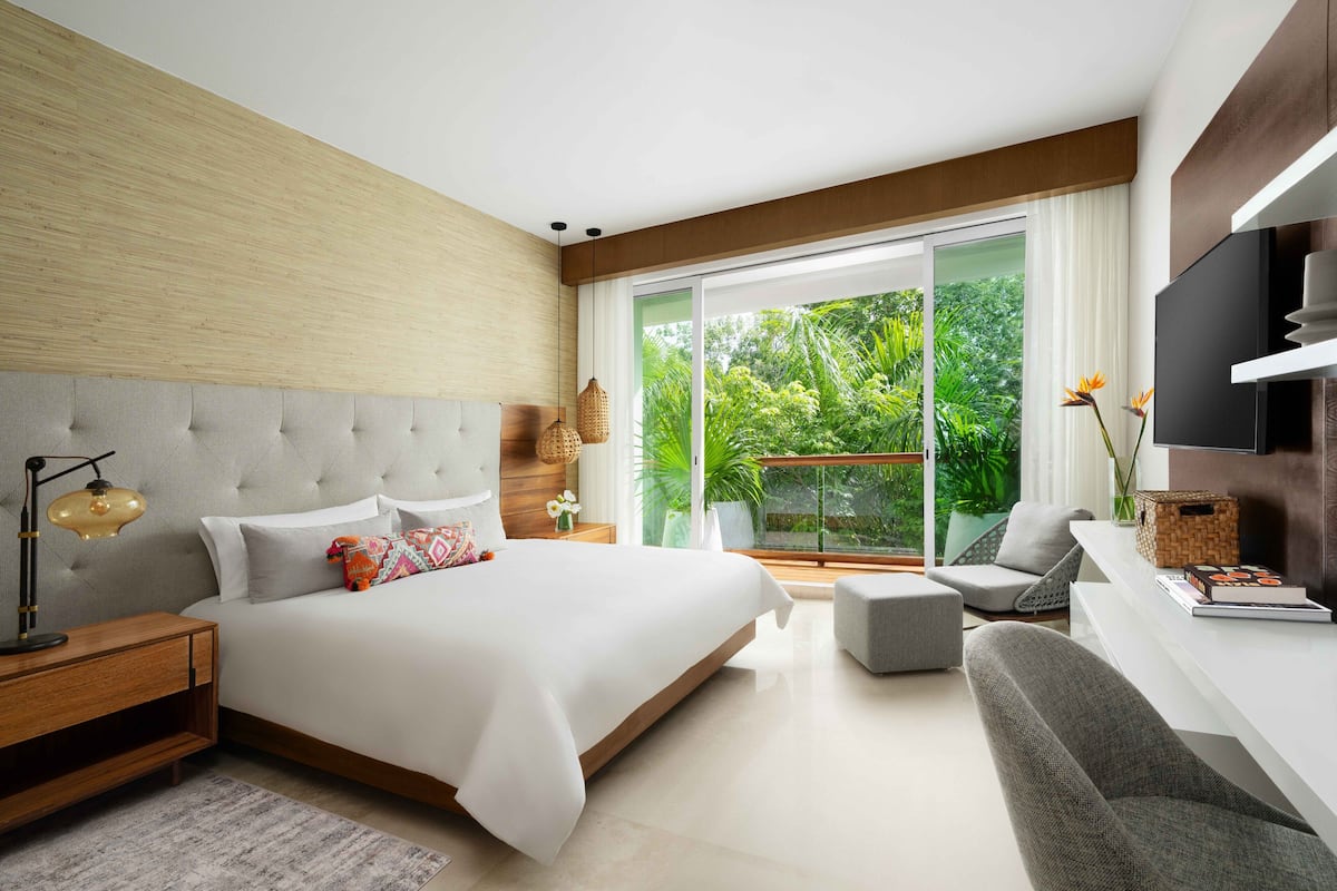 Un dormitorio moderno con una cama grande, un escritorio y vistas a zonas verdes a través de la ventana.