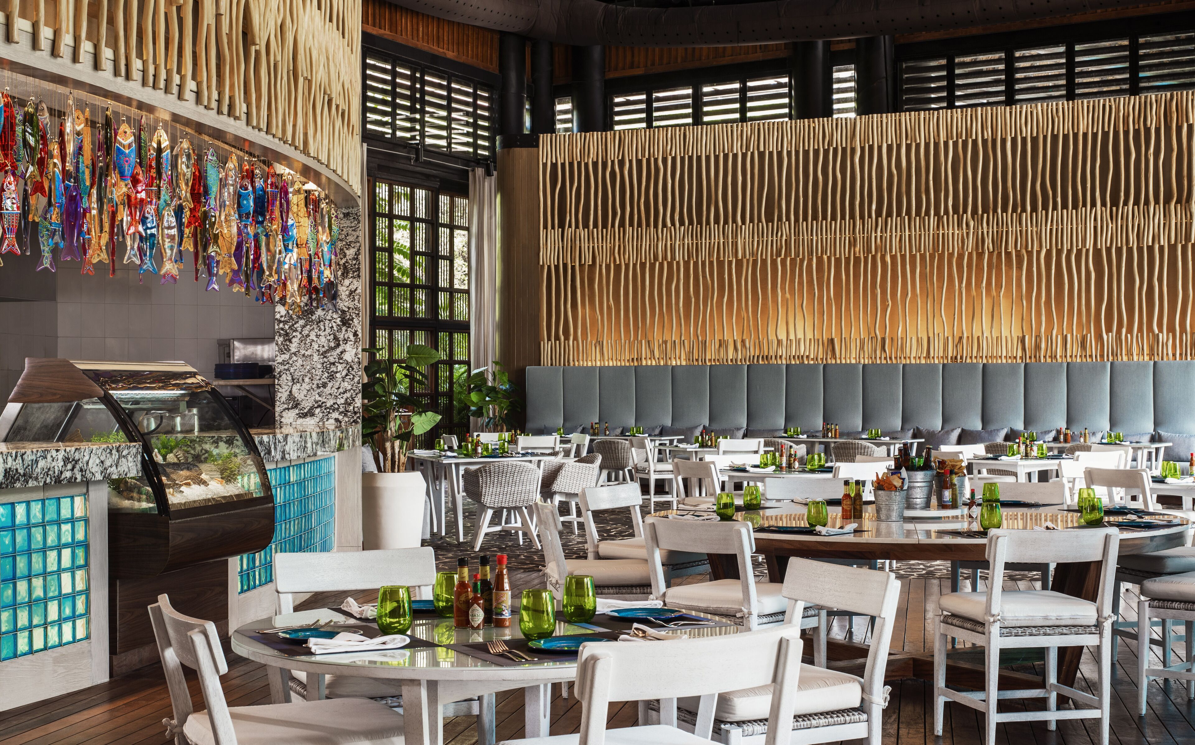 Ein Restaurant mit mehreren Tischen und Stühlen, einer Auswahl bunter Gläser und einer großen Holzwand mit vertikalen Lamellen.