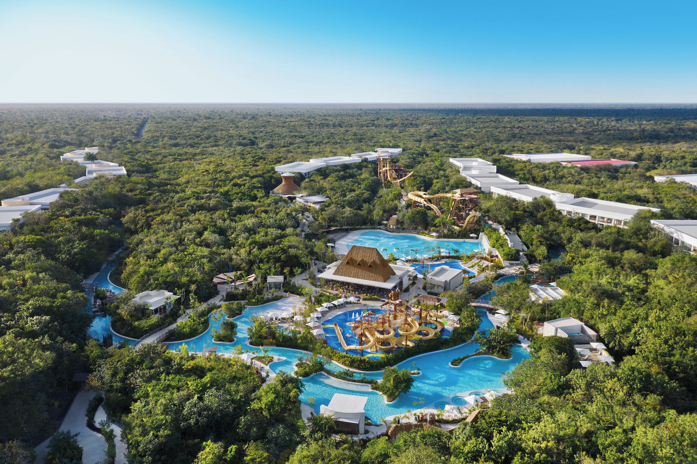 A resort with multiple swimming pools, water slides, and a large central building with a thatched roof.