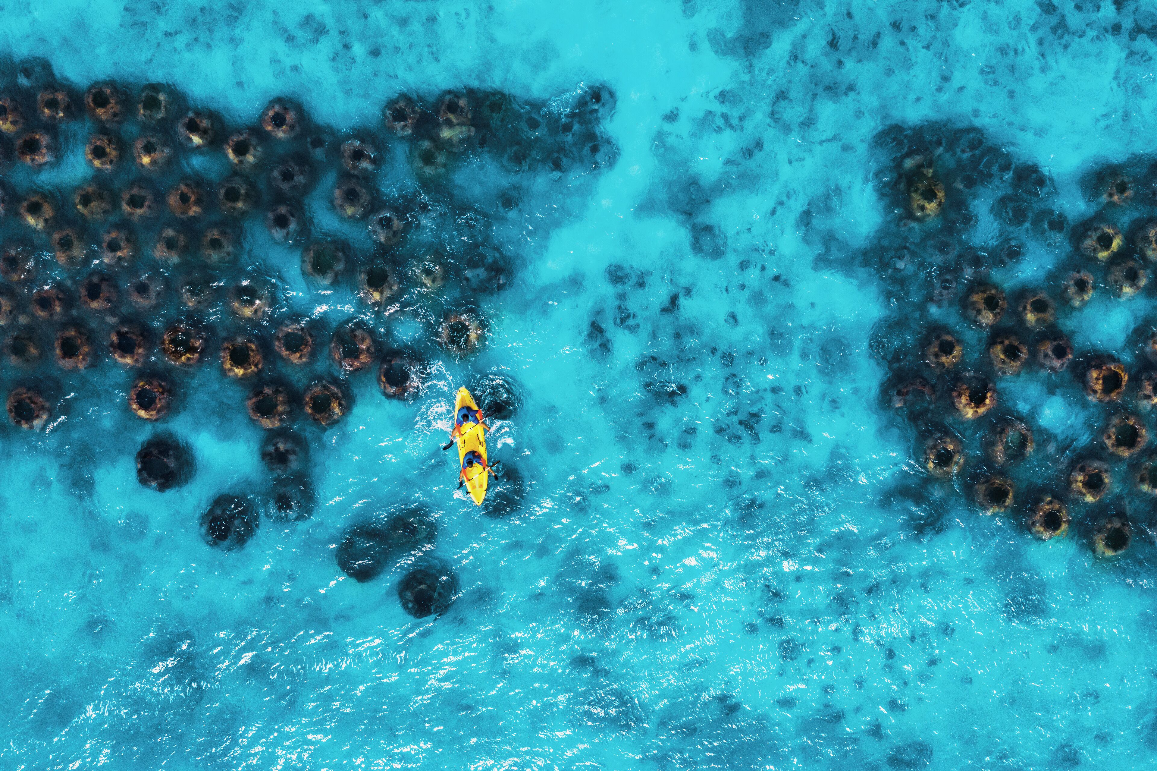 Un kayakiste dans un kayak jaune, sur une étendue d’eau parsemée de nombreux trous circulaires.