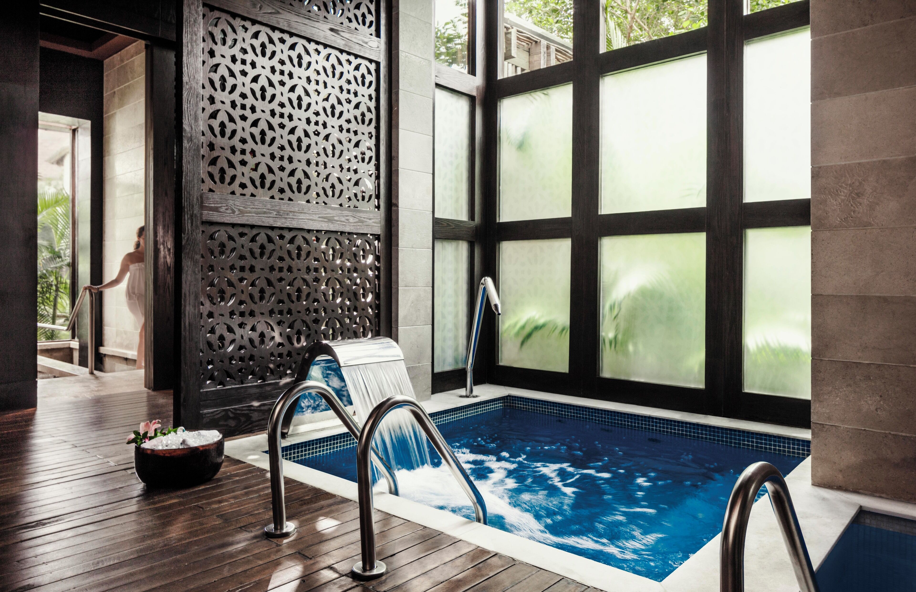 A swimming pool with a wooden deck, a decorative wall, and a view through large windows.