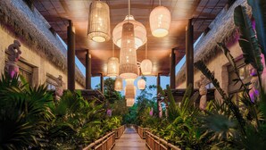 A wooden pathway flanked by lush tropical plants leading to a covered area with hanging lights. - Jungala Hotel at VidantaWorld Riviera Maya (Playa del Carmen)