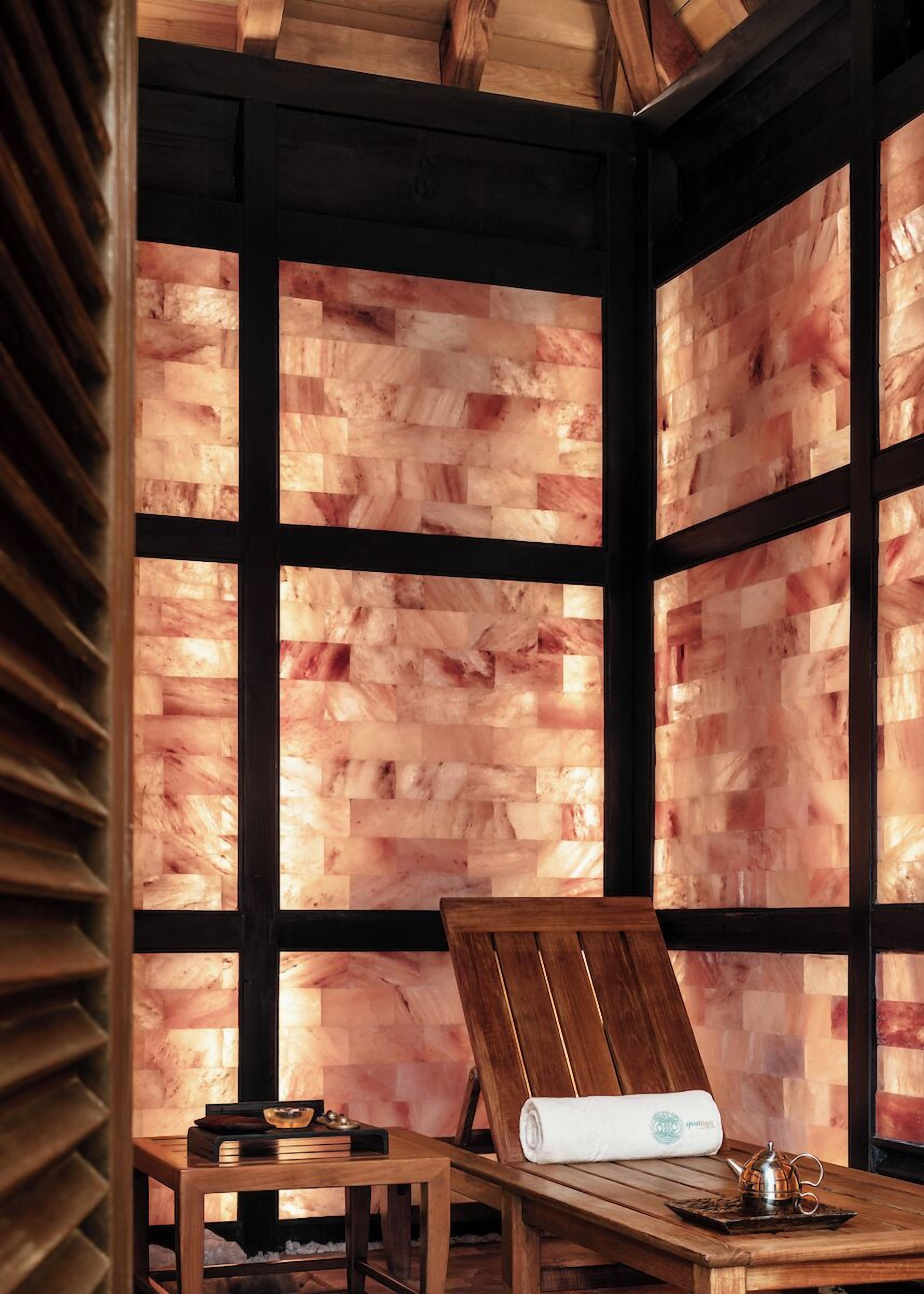 Un sauna avec des bancs en bois, une table avec une serviette et une théière, et un mur en bois doté d’une structure conçue pour retenir la chaleur.