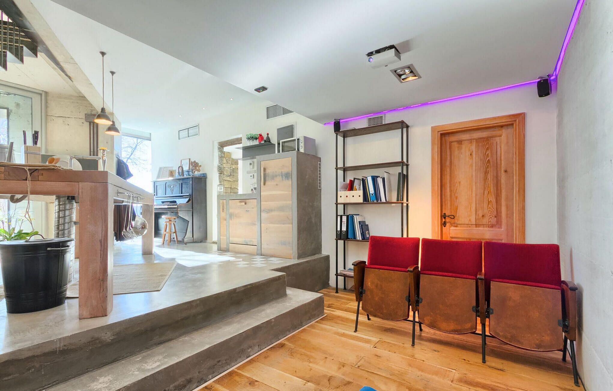 A modern kitchen with a built-in stove, a wooden dining table with red chairs, and a wooden door.