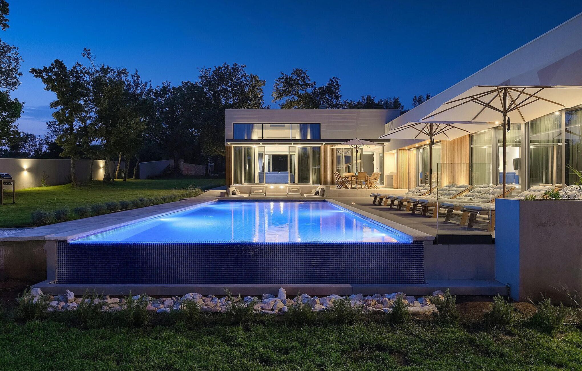 A modern house with a swimming pool, outdoor seating, and a well-lit patio area.
