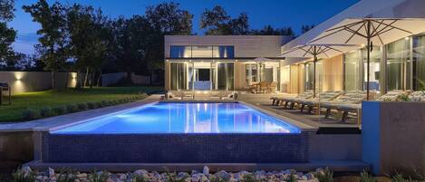 A modern house with a swimming pool, outdoor seating, and a well-lit patio area.