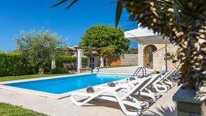 A swimming pool with lounge chairs, a pergola, and a stone building with an arched entrance. - Nice home in Porec with sauna (Porec)