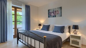 A bedroom with a bed, two bedside tables, a window with curtains, and a painting on the wall. - Nice home in Porec with sauna (Porec)