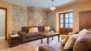 A living room with a stone wall, a brown sofa set, a wooden coffee table, and a large window with frosted glass panels. - Nice home in Porec with sauna (Porec)