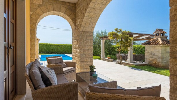 A covered outdoor seating area with wicker furniture, a stone archway, a pool, and a pergola with a tiled roof. - Nice home in Porec with sauna (Porec)