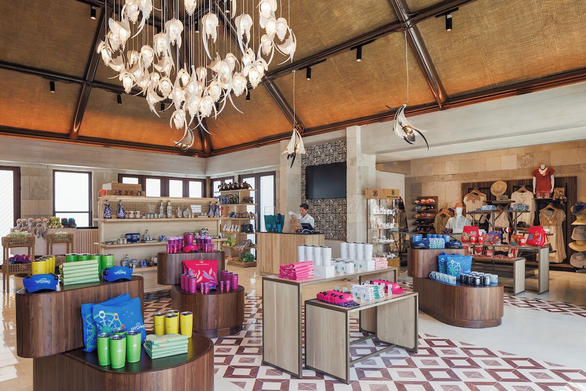 Un espacioso hall de hotel boutique con mobiliario de madera, suelo estampado y diversas vitrinas de venta al público.
