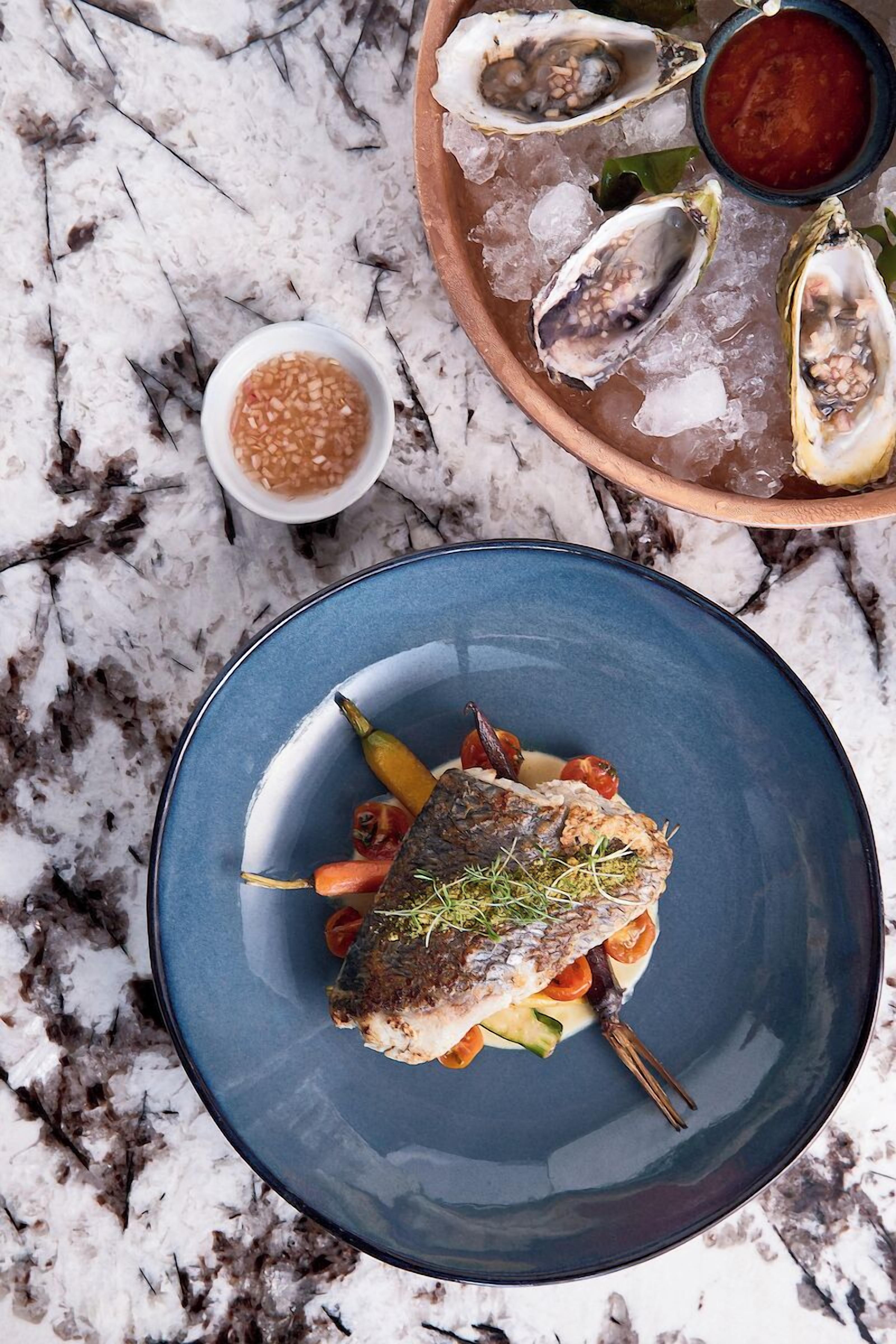 A seafood dish with a fish, vegetables, and herbs on a blue plate.