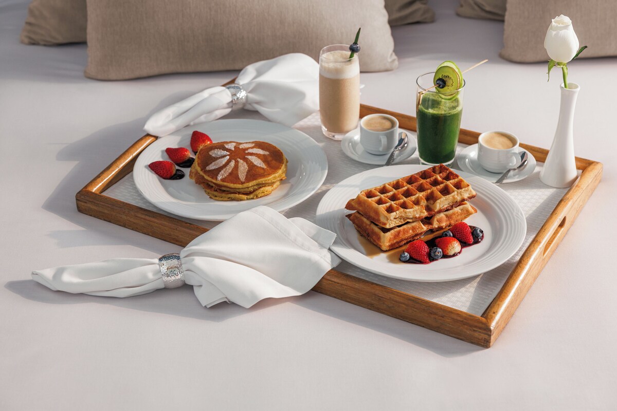 Un plateau de petit-déjeuner avec des crêpes, des gaufres et des fruits rouges frais, disposés sur un lit.