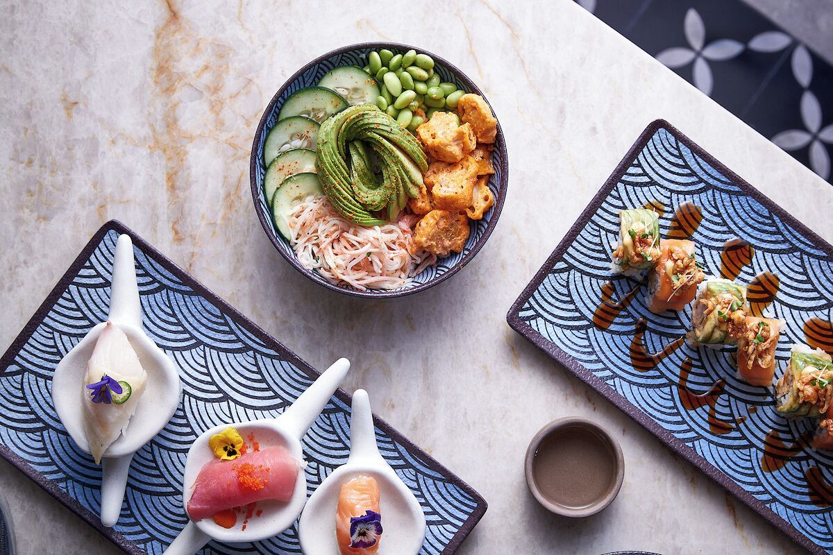 Diverse gerechten op een tafel, waaronder sushi, sashimi en een saladekom met komkommer en edamame.