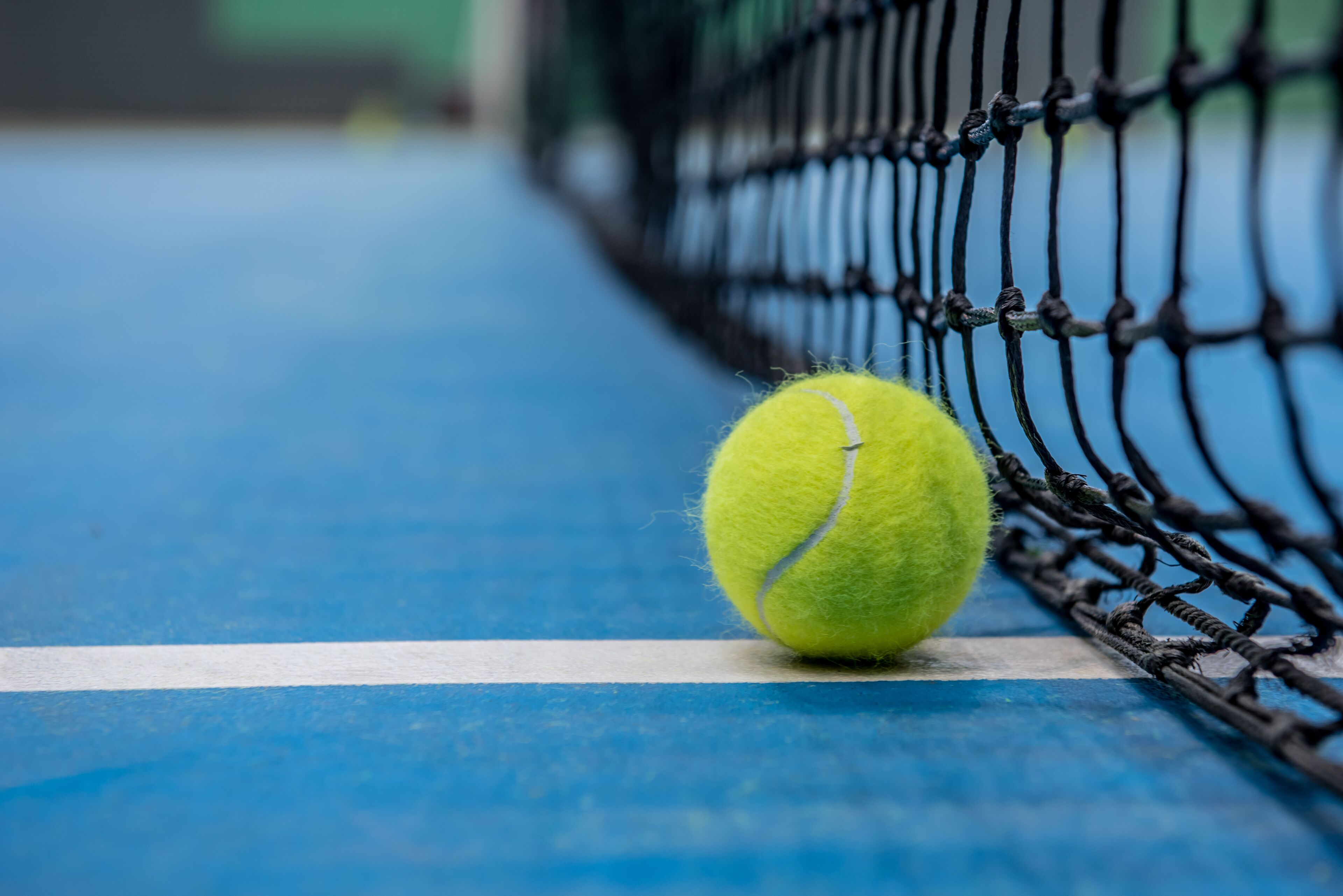 A tennis ball on a blue court near a net.