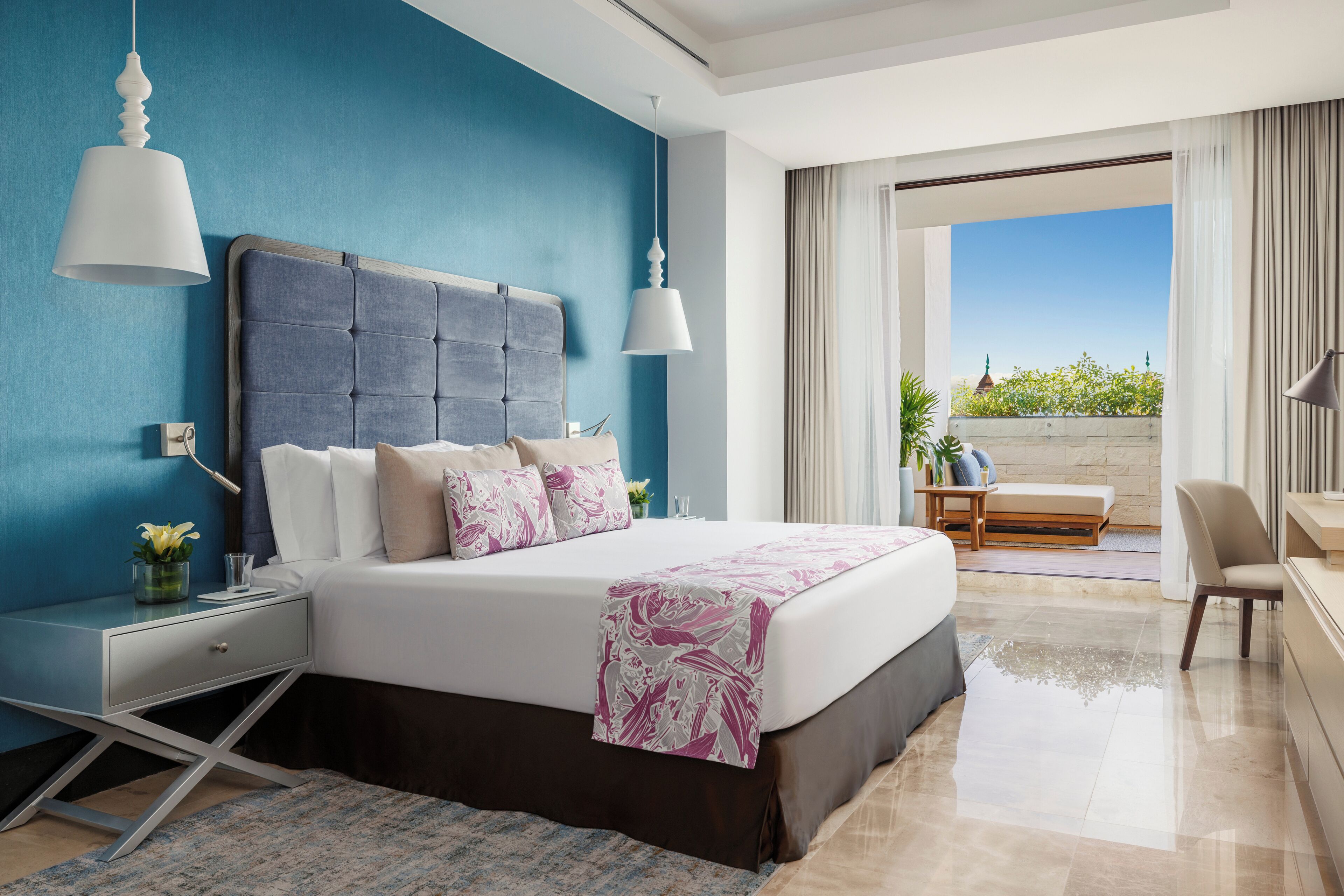 A modern hotel room with a large bed, a nightstand, a desk, and a view of the outdoors.