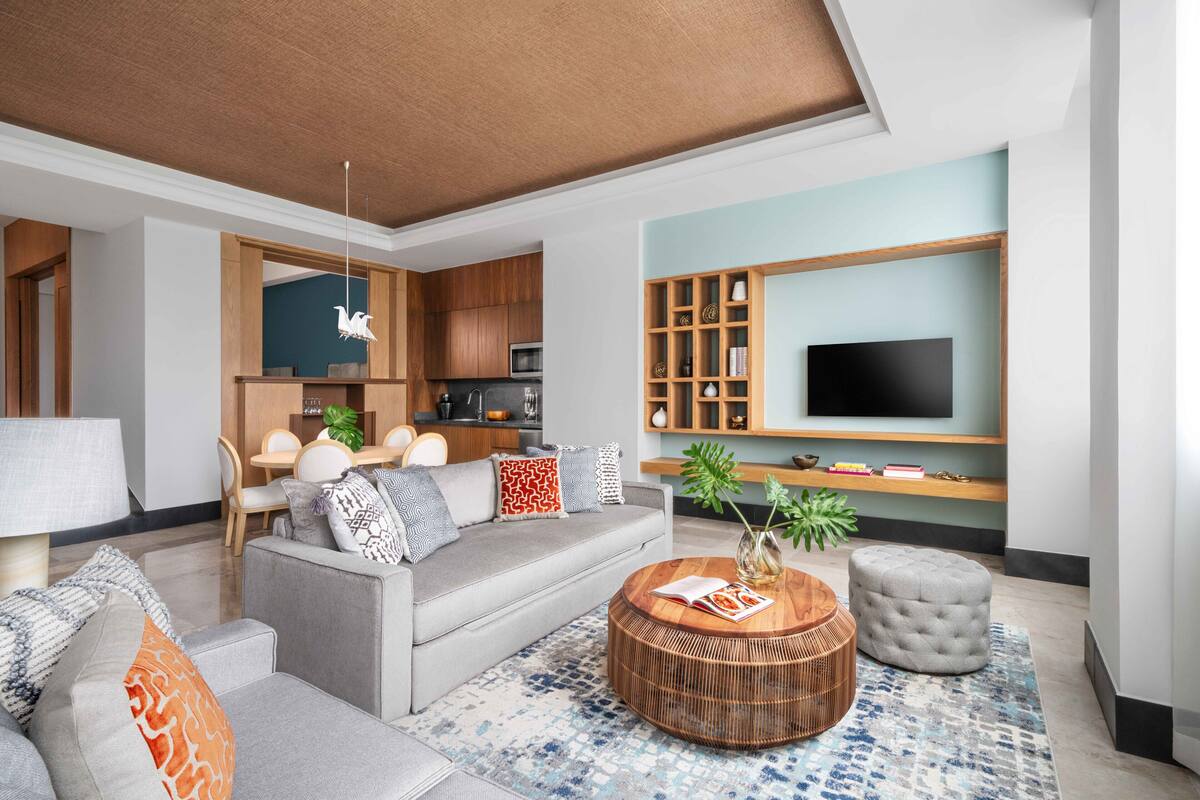 En moderne stue med sofa, sofabord, skammel og et fladskærms-tv på væggen.