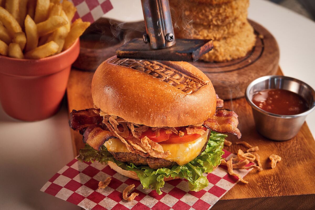 A burger with bacon, cheese, lettuce, and fried onions, served on a checkered paper.