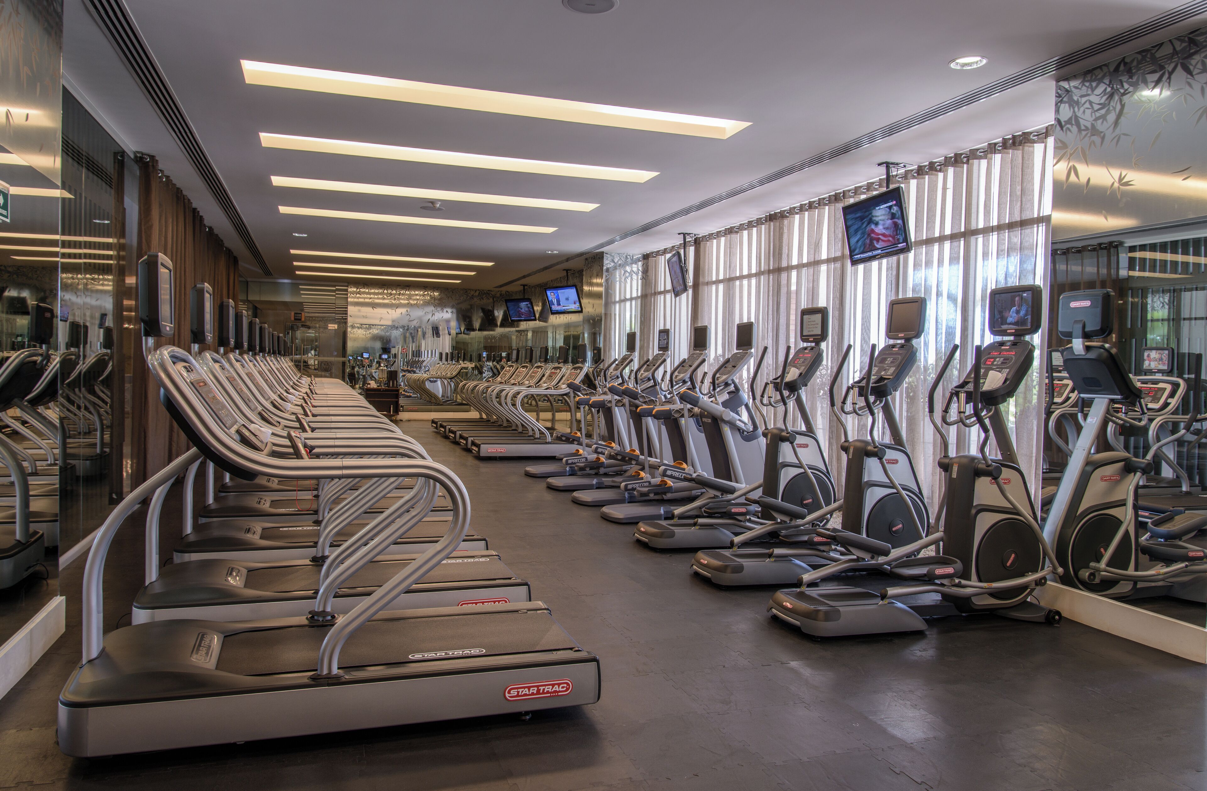 A gym with multiple treadmills and elliptical machines arranged in rows.