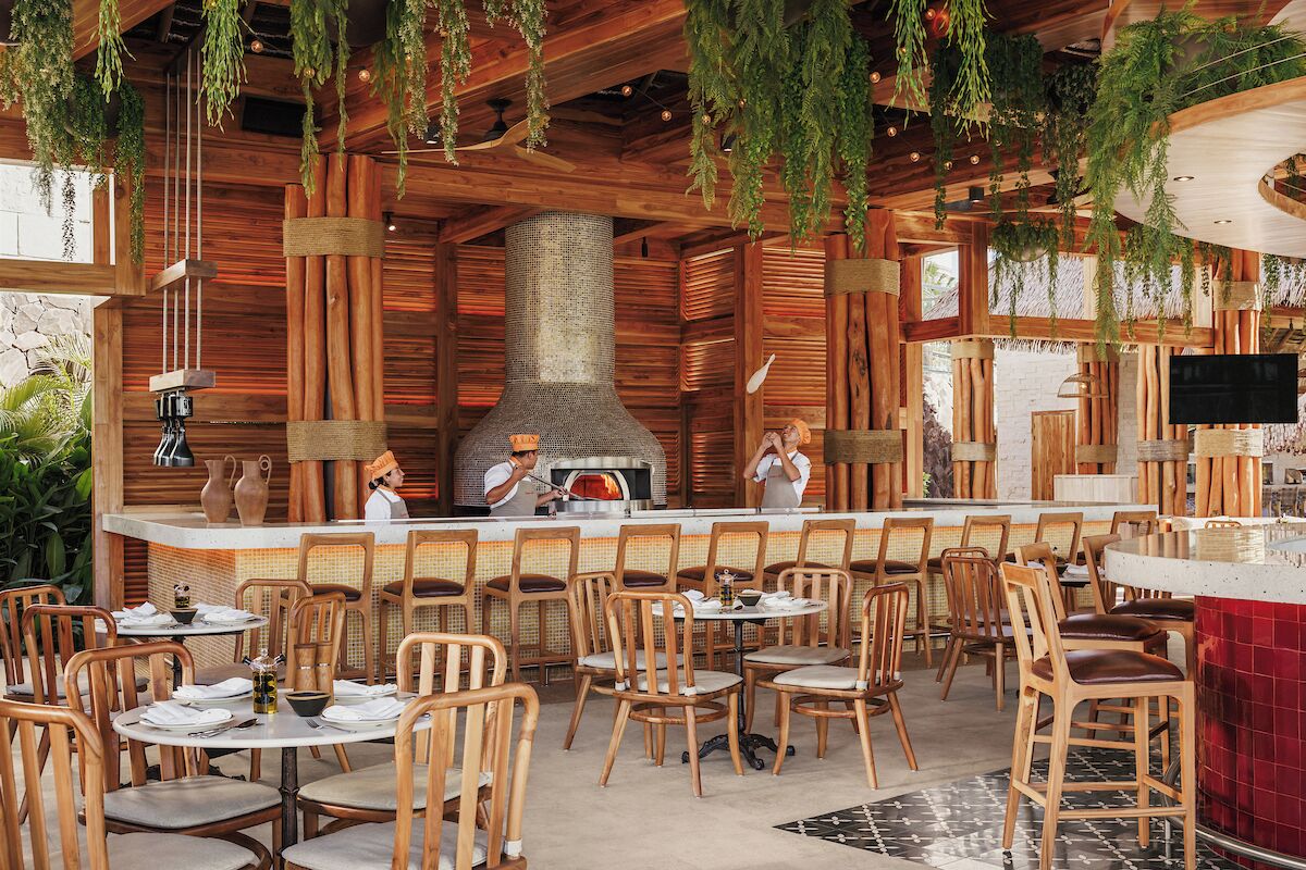 A restaurant with wooden interior, hanging plants, and a central cooking area.