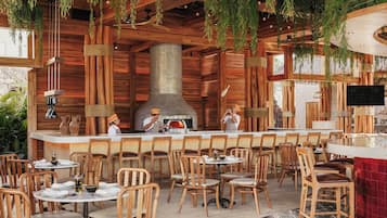 A restaurant with wooden interior, hanging plants, and a central cooking area.