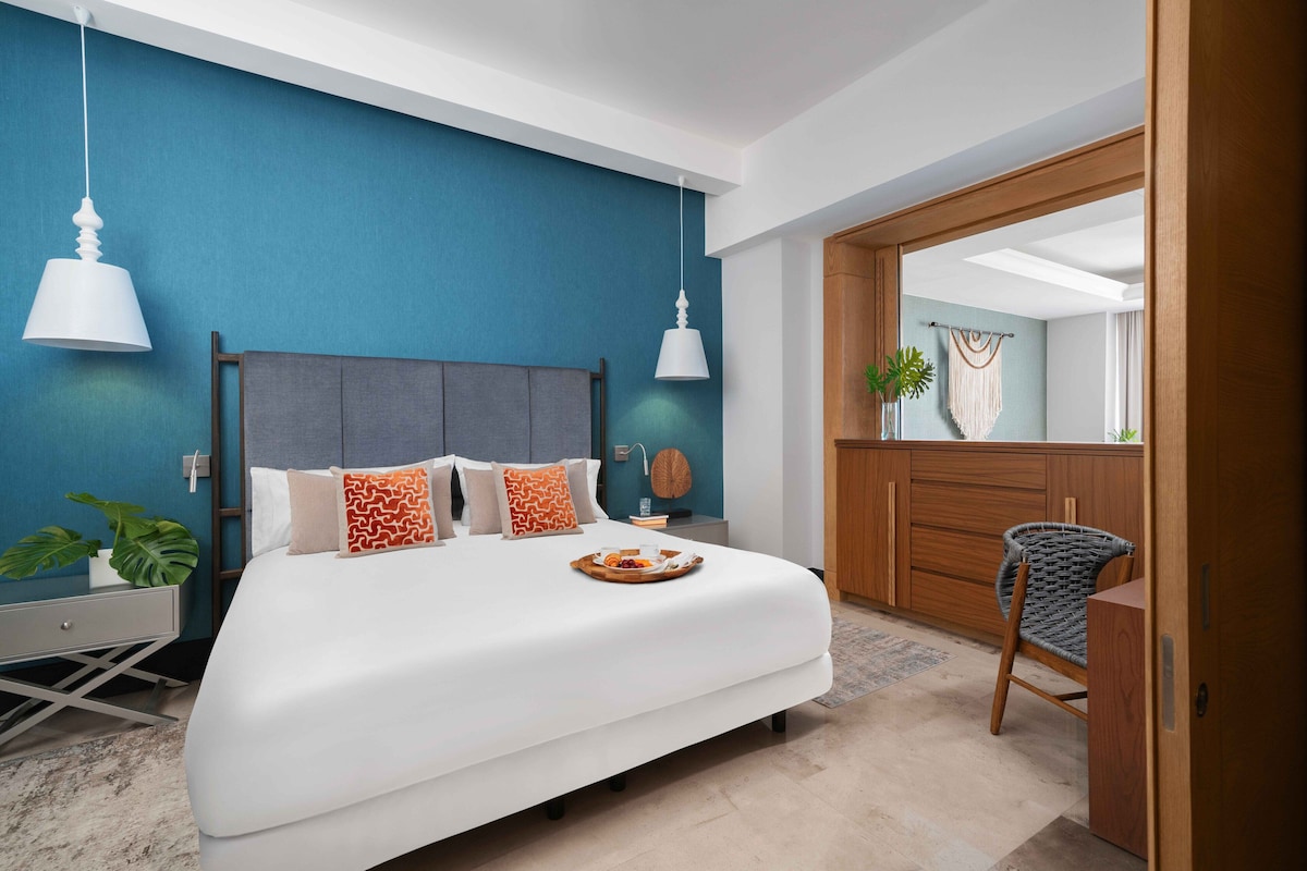 Een moderne slaapkamer met een groot bed, twee hanglampen, een houten garderobe en een spiegel.