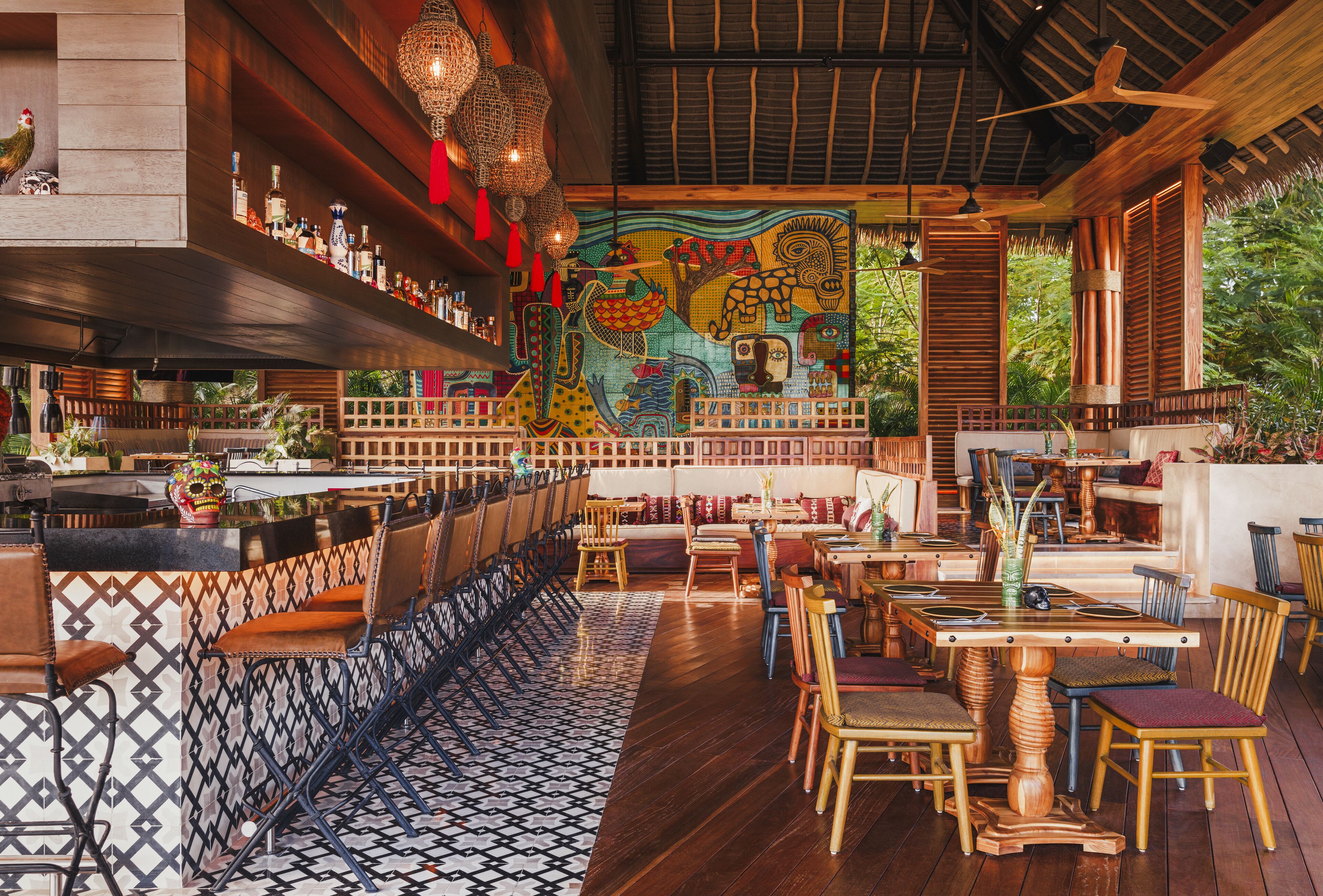 Un restaurante con zona de bar, muebles de madera y un mural colorido en la pared.