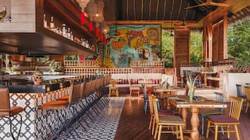 Un restaurante con zona de bar, muebles de madera y un mural colorido en la pared.