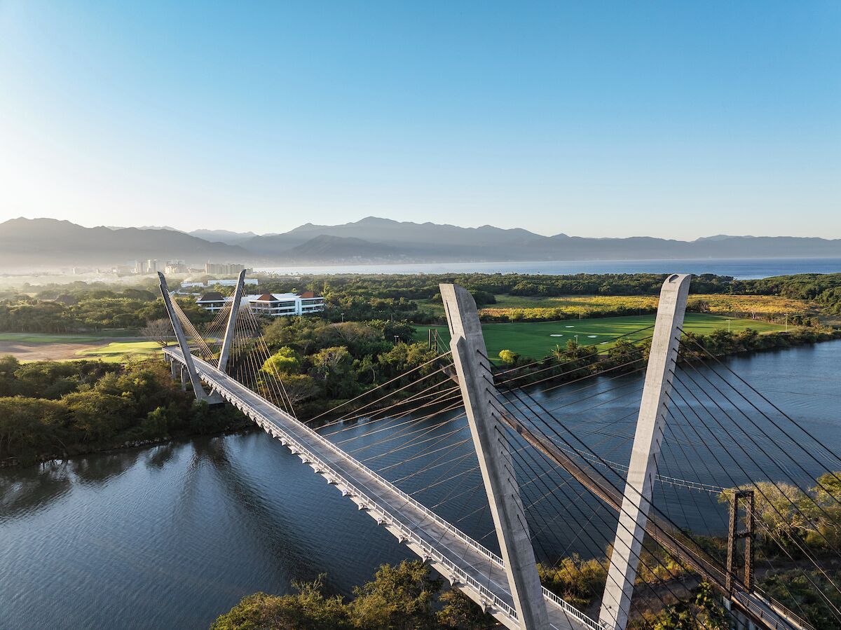 A cable-stayed bridge with a clear view of the surrounding landscape, including a river and distant mountains.