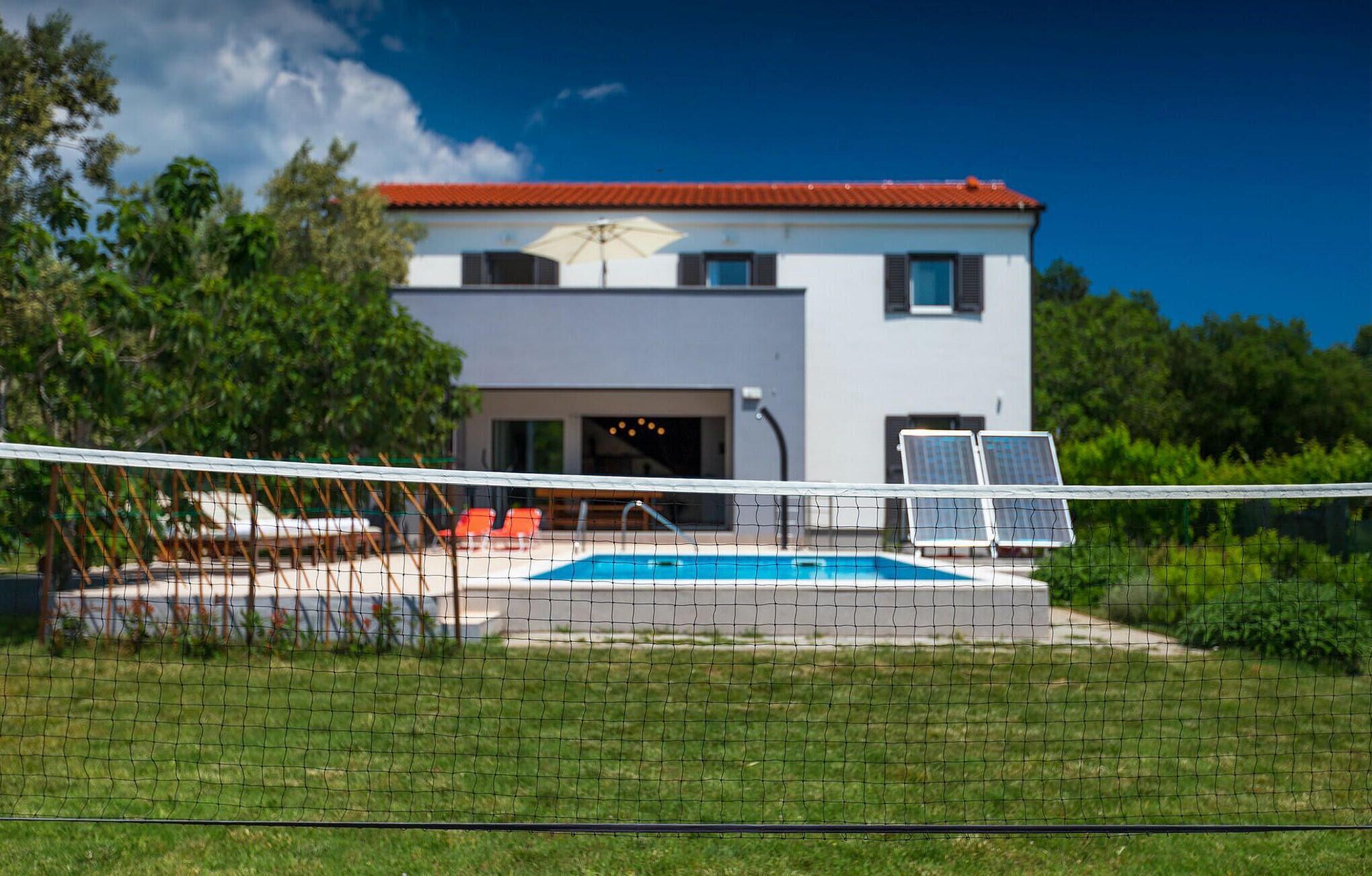 A modern two-story building with a swimming pool, solar panels, and a covered seating area.
