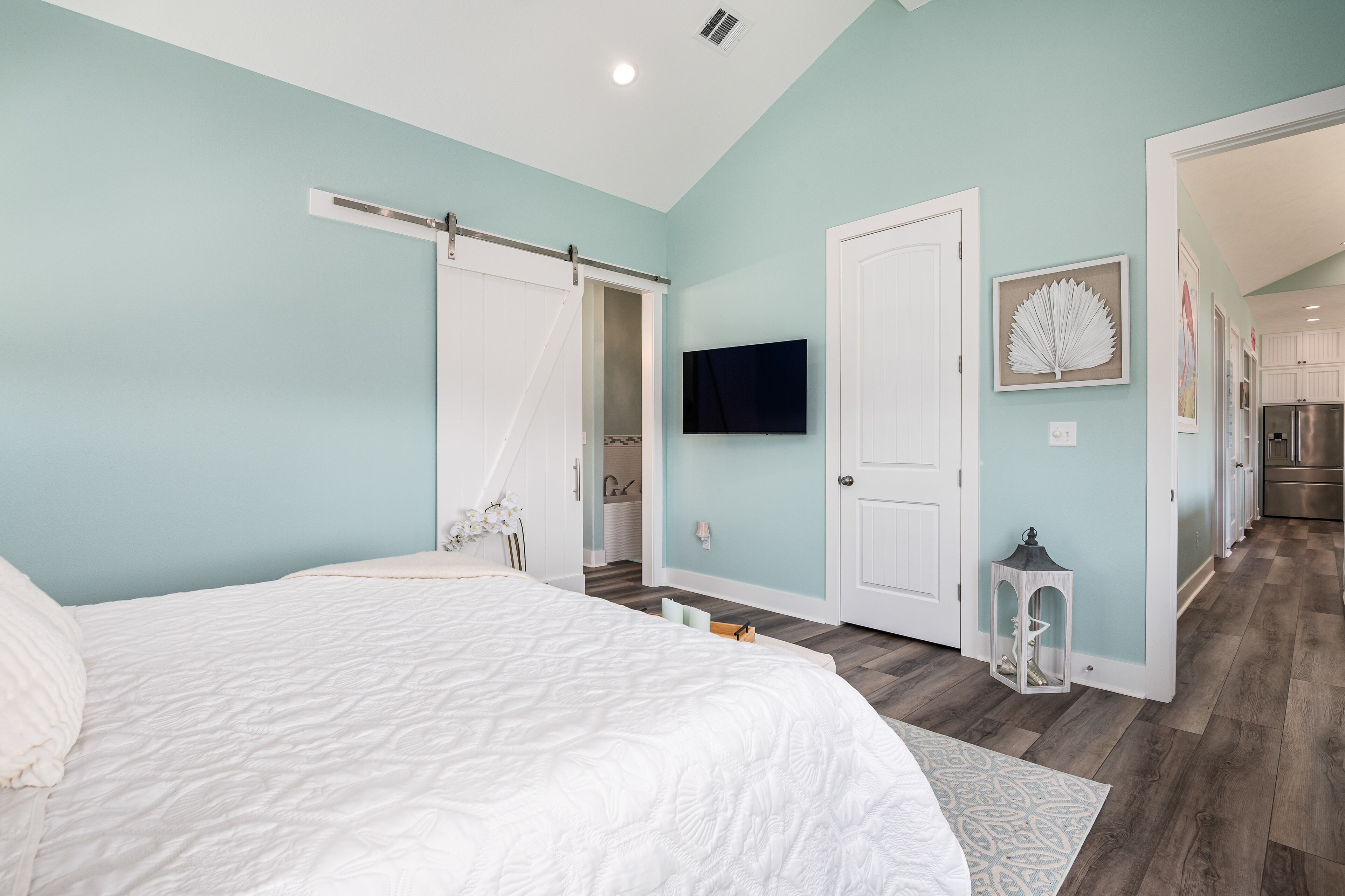 Une chambre à coucher comprenant un lit, une porte coulissante, un téléviseur et un couloir menant à la cuisine.